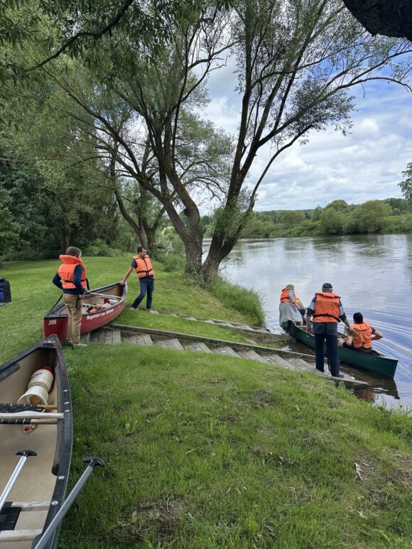 Personen in Rettungswesten tragen zwei Kanus ins Wasser